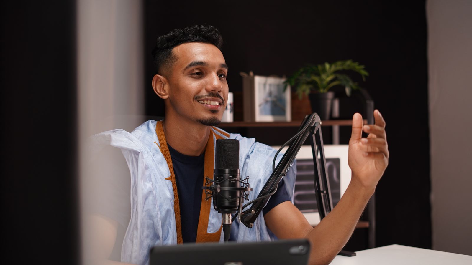 Presenter seated at a lit studio desk speaking directly to camera